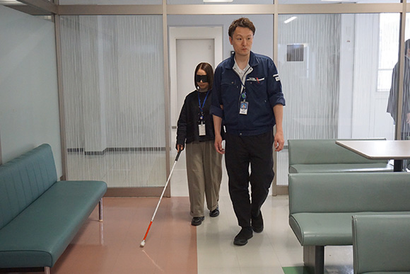 アイマスクを着用し白杖を持って立っている人